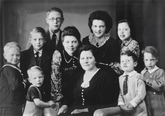 Familieportret, moeder met de negen kinderen, rechtsvoor met stropdas zit Bas.
